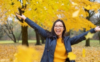 A happy person outside surrounded by yellow leaves.