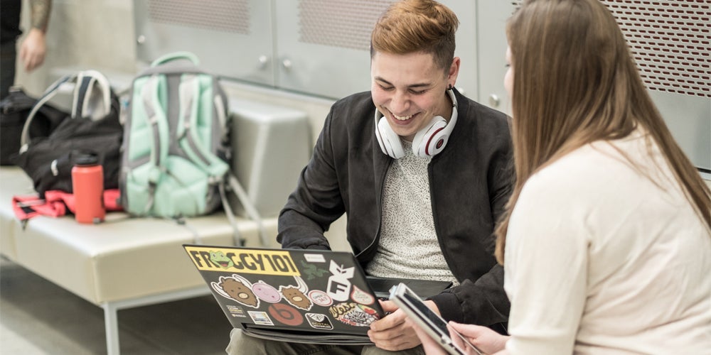 two students talking and laughing while looking at a laptop