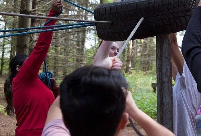 A group of students hoist a tire in the air in a forest