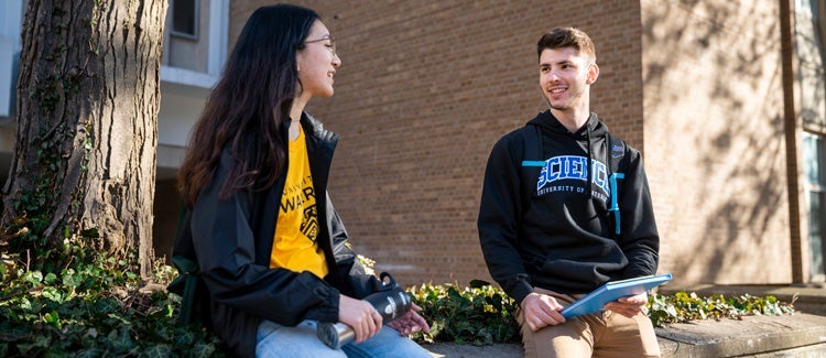 Two students leaning on short wall outside