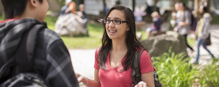 Student in red shirt and glass talks to another student