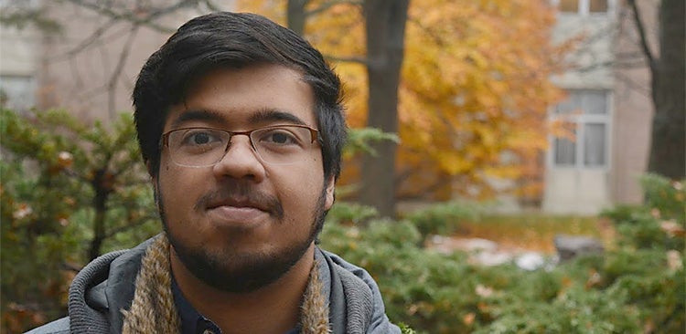 Student standing outside with fall colours behind him