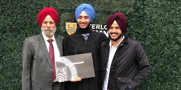 Dr. Singh, Harkanwal, and Jasmeet at Harkanwal’s graduation in front of a green background and and a sign that says #UWaterlooGrad