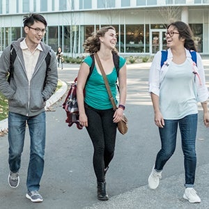 Three students wearing backpacks with building in background