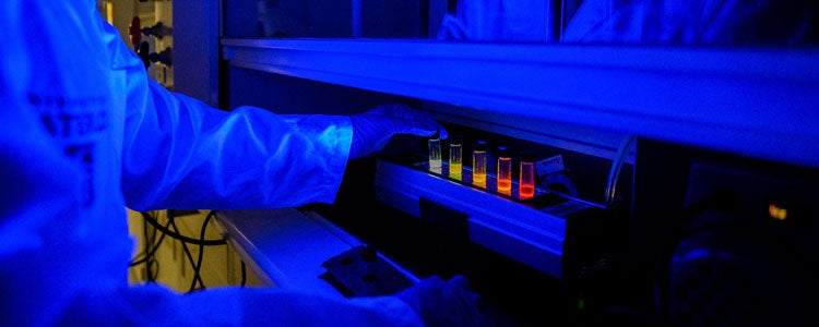 Student wearing lab coat handling colourful test tubes in a dark room