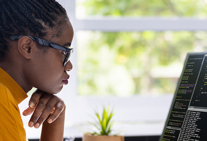 Person wearing glasses working at a laptop on a desk displaying software code.