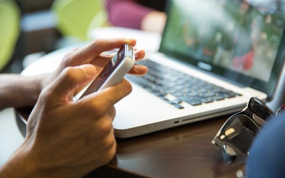 Close up of hands using a phone with laptop in background