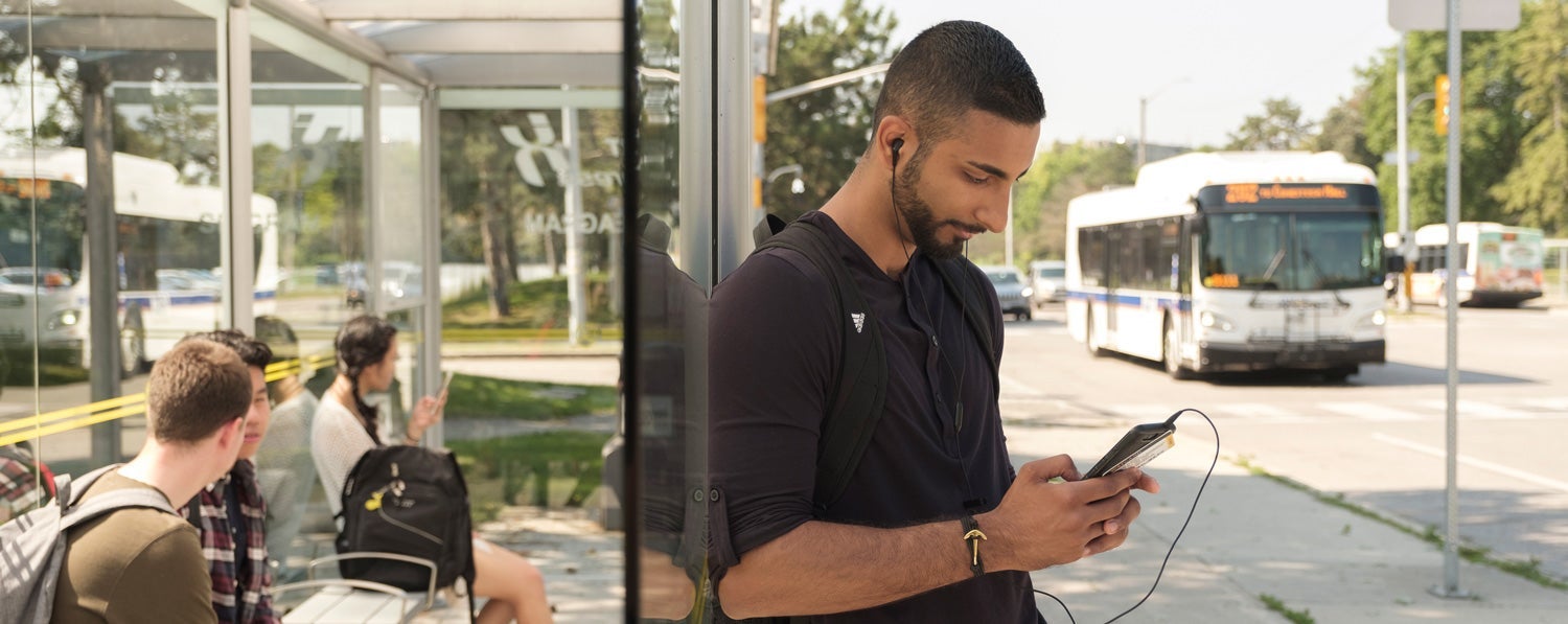 student standing at bus stop looking at phone