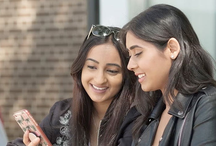 Two students sitting outside look at a phone