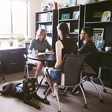 Two students talking with accessibility services while sitting down with a service dog