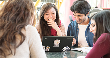 students conversing and smiling at a laptop