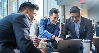 Students in suit jackets point at something on their laptop