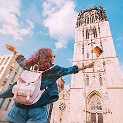 A woman spreads her arms while looking up at a historical building