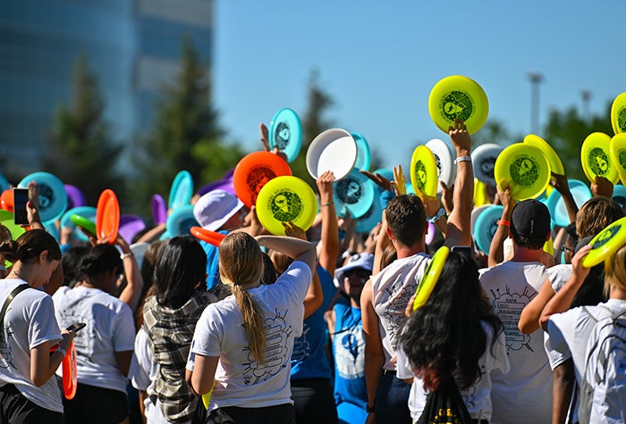 students in a group outside holding coloured frisbees in their air