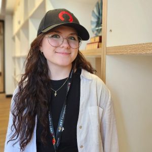 Taylor wears a baseball cap and glasses and smiles