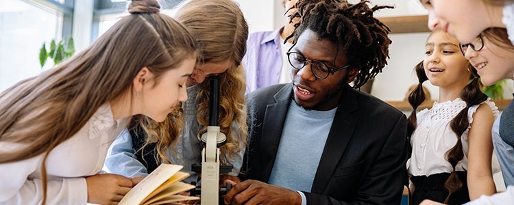 A teacher helps students look through a microscope