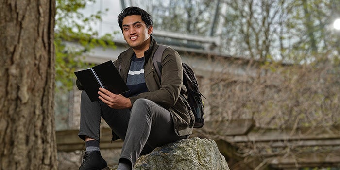 Student sitting on a rock, holding a notebook