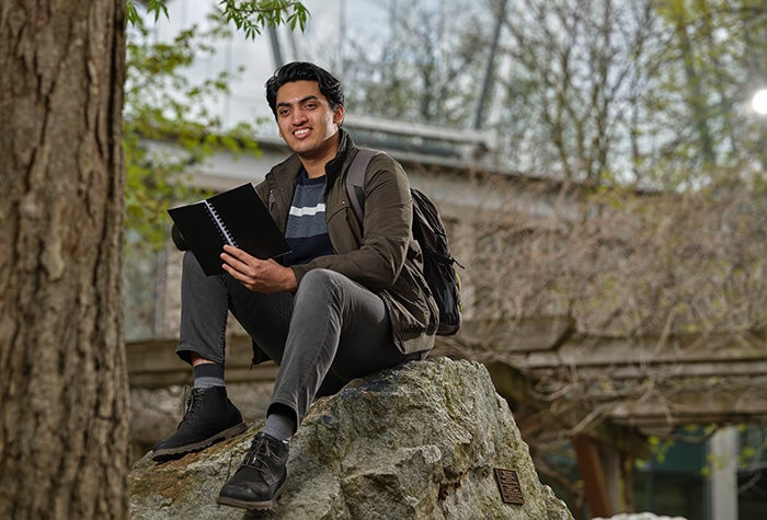 Student sitting on a rock and reading a book