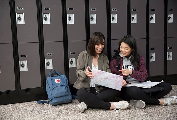 two students sitting against lockers