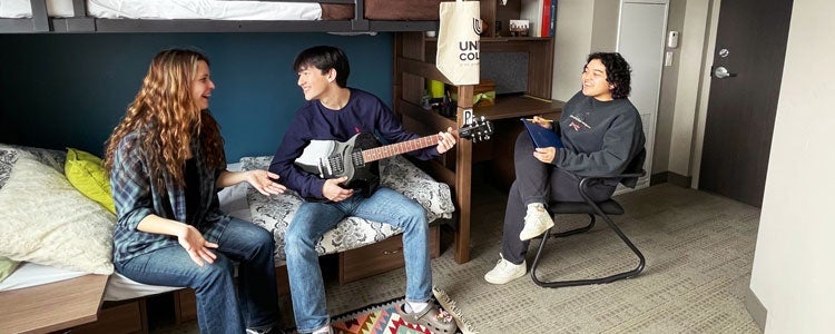 Waterloo students in a United College residence room. One student is playing guitar.