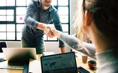 Two people shaking hands across a desk.