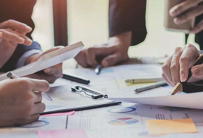 A table with lots of paper and supplies and hands using them
