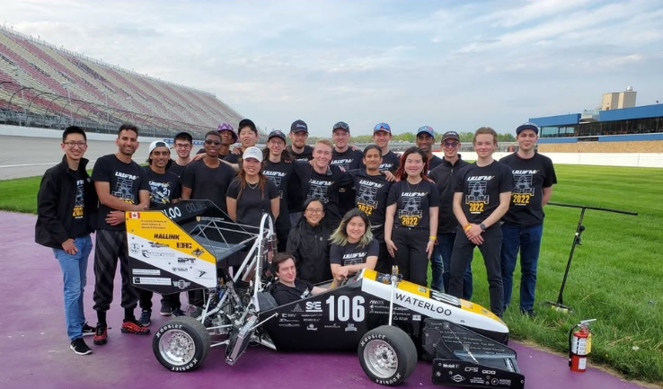 Students gather around a person sitting in the race car they designed and manufactured.