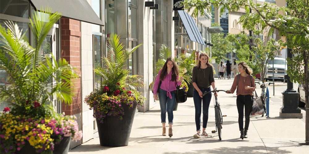 three students walking down residential street, one with a bicycle