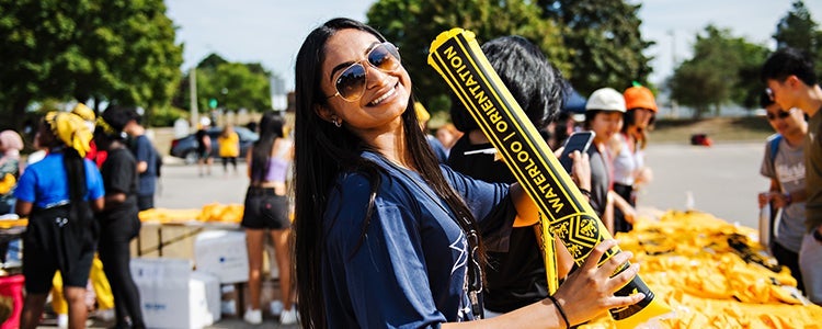 happy student standing in an orientation crowd holding Waterloo inflated sign