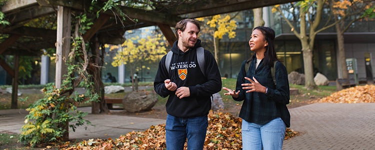 Two students walking and talking on campus in the fall