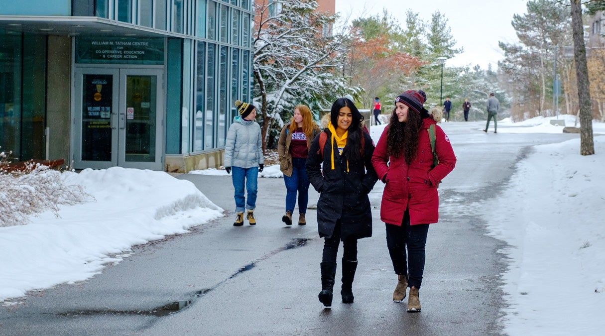 Students in winter coats walk along snowy path at the University of Waterloo