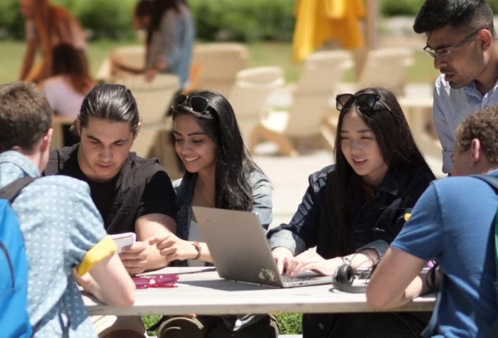 A group of students working together on a table outside on campus.