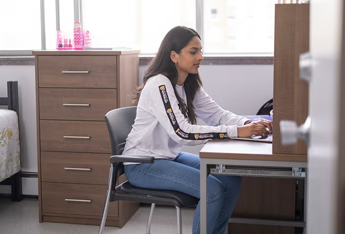 Student sitting at her desk in her room in residence.