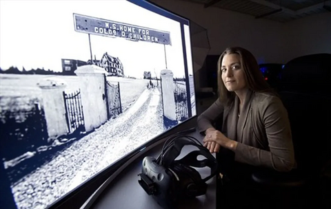 Kristina standing in front of a photo of the NSHCC with a VR headset 