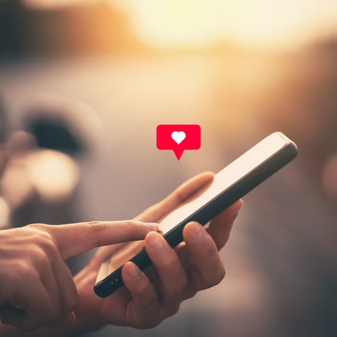 Cell phone with heart emoji above it.