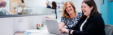 Dr. Diana Parry and student smiling as they review work on a laptop.