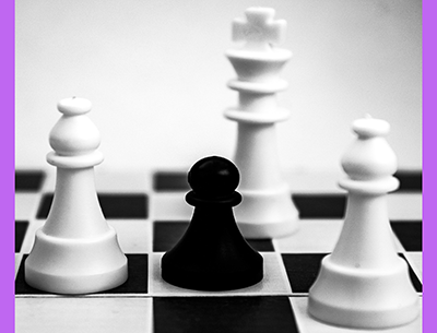 black pawn on a chess board surrounded by white king and bishops