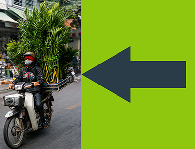 A person riding a motorcycle with plants on the back, wearing a shirt with a Union Jack on it and a mask