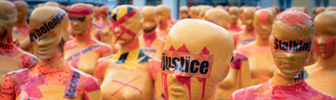 orange mannequins wrapped in caution tape with words "justice" over their eyes
