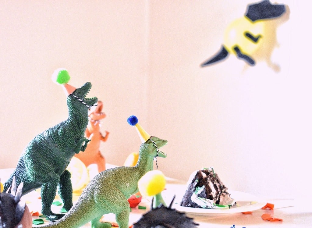 toy dinosaurs in party hats on a table with a piece of cake