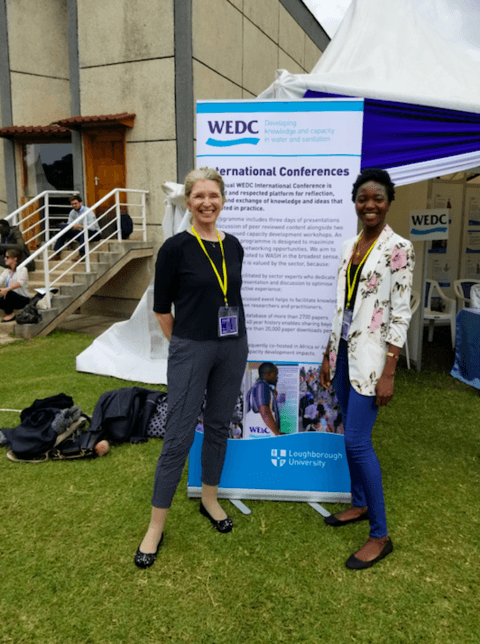 Dr. Susan Elliott and PhD student Thelma Abu stand beside WEDC conference banner