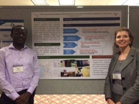 Susan and Elijah standing beside their conference poster