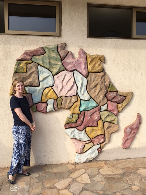 Susan stands beside a handmade map of Africa depicted on the side of a building