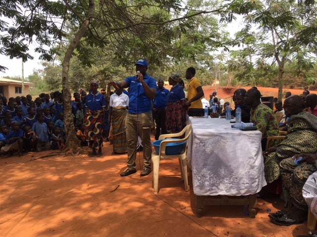 A male teacher addresses a class of students outside in Ghana