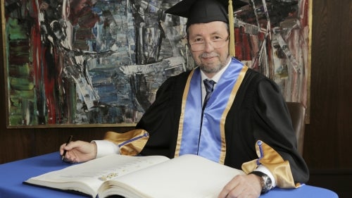 Dean Roy wearing academic regalia while signing register