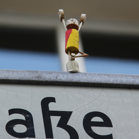 Small figurine, painted in German colours, built out of cork, perched on top of a sign