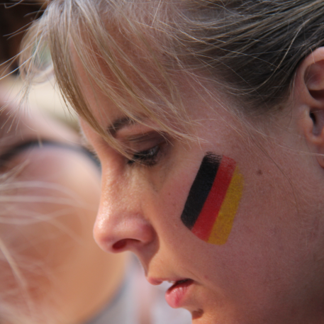 Close-up of a woman's face. Painted on her cheek is a German flag