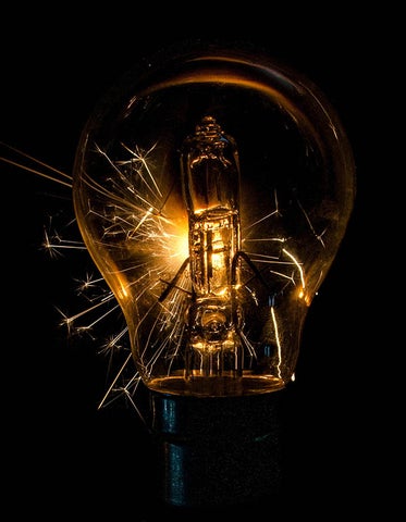 The outline of a light bulb with sparks shooting from it glows against a black background