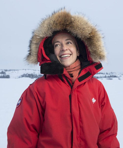Courtney Howard wearing a red parka with a fur lined hood, standing outside in a winter landscape.
