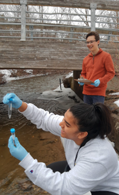 Student collecting water sample with second student watching